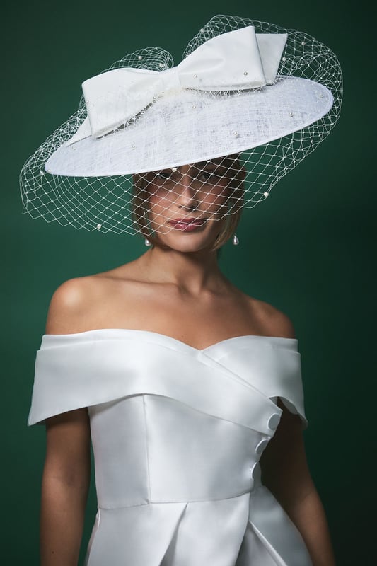 Striking wide brim fascinator with delicate pearl-adorned veil for a romantic finish
        Statement bow detail adds a contemporary touch to this classic bridal accessory
        Textured fabric base provides structure and sophistication
        Lightweight design ensures comfort throughout your special day
        Secures easily with discreet attachments for worry-free wear
    
    Make a captivating entrance on your wedding day with this exquisite Lisa Tan bridal fascinator from Coast. The wide brim silhouette creates a dramatic yet elegant profile, whilst the delicate veil adorned with subtle pearls adds a touch of romance and tradition. The statement bow detail introduces a modern twist to this timeless accessory, perfectly complementing an off-shoulder wedding gown as shown. This versatile piece works beautifully with both classic updos and flowing locks, allowing you to create your desired bridal aesthetic. Beyond the ceremony, this fascinator transitions seamlessly to the reception, maintaining its graceful presence throughout your celebrations. Pair with minimal jewellery to let this showstopping headpiece command attention, or match with pearl accessories for a coordinated bridal ensemble that reflects sophisticated British wedding style.