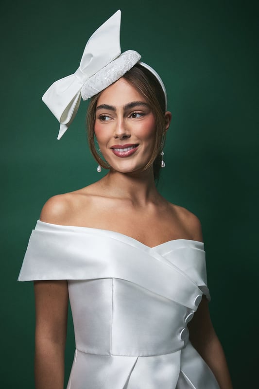 Elegant pillbox fascinator featuring a statement oversized bow detail
        Delicate lace detailing with subtle sequin embellishment for a touch of sparkle
        Secure headband design ensures comfortable wear throughout your special day
        Handcrafted from lightweight Abaca material for all-day comfort
        Versatile positioning allows for personalised styling to complement your bridal look
    
    Make a sophisticated statement on your wedding day with this exquisite Lisa Tan bridal fascinator. The classic pillbox silhouette is beautifully modernised with an eye-catching bow that adds dramatic flair without overwhelming your bridal ensemble. The intricate lace detailing creates a textural contrast against the smooth bow, offering a perfect balance of traditional craftsmanship and contemporary design. Style with an off-shoulder wedding gown as shown for a harmonious bridal aesthetic, or pair with a sleek updo to showcase dangling earrings for added glamour. This fascinator works beautifully with both classic and modern bridal styles, offering the perfect finishing touch whether you're walking down the aisle, posing for photographs, or celebrating at your reception. The secure fit ensures you can dance the night away with confidence.