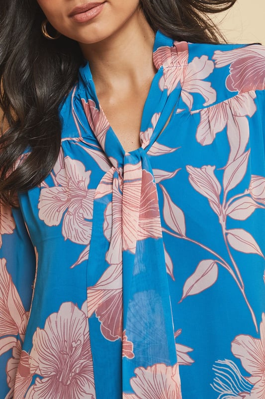 Elegant tie neck detail creates a sophisticated silhouette
        Striking floral print adds visual interest to your daywear collection
        V-neckline frames the face beautifully
        Long sleeves with subtle gathering for a feminine touch
        Regular fit ensures comfortable all-day wear
    
    This captivating floral print blouse from Wallis combines effortless style with versatility. The elegant tie neck detail allows you to customise your look-wear it loosely draped for casual gatherings or neatly tied for a more polished appearance. Style with wide-leg denim trousers as shown for a contemporary daytime ensemble, perfect for lunch with friends or weekend shopping trips. The lightweight woven fabric drapes beautifully, creating movement as you walk. For cooler days, layer under a tailored blazer or casual cardigan. Complete your look with hoop earrings and ankle boots for an outfit that transitions seamlessly from family brunches to informal dinner dates. This blouse offers the perfect balance of comfort and sophistication for the woman who appreciates glamour in her everyday wardrobe.