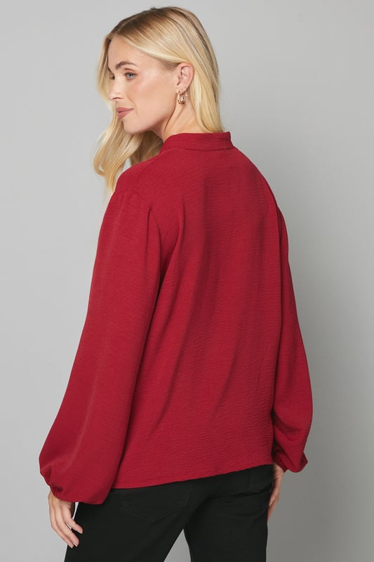 Elegant collarless design with a flattering V-neckline
        Relaxed silhouette with full-length sleeves for sophisticated comfort
        Lightweight woven fabric that drapes beautifully
        Versatile blouse perfect for creating both casual and smart looks
        Petite fit designed specifically for smaller frames
    
    This Wallis collarless blouse combines effortless style with day-to-day versatility. The clean lines and absence of a traditional collar create a modern, streamlined look that's both sophisticated and relaxed. Style with leather-look trousers and ankle boots for a contemporary daytime ensemble, or pair with tailored wide-leg trousers and ballet flats for family gatherings. The flowing fabric and comfortable regular fit make this blouse ideal for long days at the office or weekend brunches with friends. Add a structured tote and simple gold-toned jewellery to complete your look. This wardrobe essential transitions seamlessly from desk to dinner, offering endless styling possibilities whilst maintaining that signature Wallis glamour that doesn't compromise on comfort.