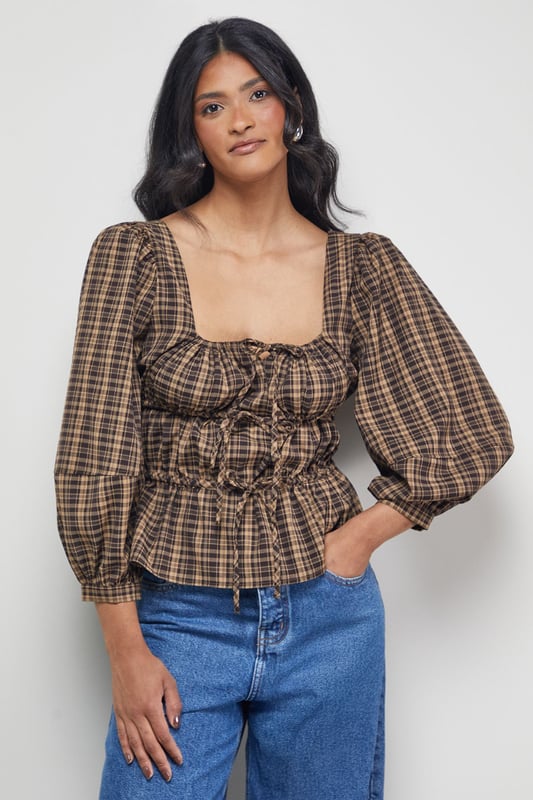 Elegant square neckline with charming tie-front detail
        Voluminous balloon sleeves for a dramatic silhouette
        Fitted smocked bodice creating a flattering shape
        Classic check pattern offering timeless appeal
        Peplum-style hem adding feminine flair to your outfit
    
    This Warehouse blouse combines vintage-inspired charm with contemporary styling. The square neckline frames your dcolletage beautifully, while the tie-front detail adds a touch of playful femininity. The smocked bodice creates definition at the waist, contrasting perfectly with the billowing sleeves for a balanced silhouette. Style with wide-leg jeans and ankle boots for casual weekend brunches, or tuck into a high-waisted midi skirt for family gatherings. For a more polished daytime look, pair with tailored trousers and loafers. The versatile check pattern works brilliantly across seasons - layer under a cardigan when temperatures drop or wear alone for warmer days. This blouse effortlessly bridges the gap between casual comfort and put-together style, making it a wardrobe essential for the confident woman.