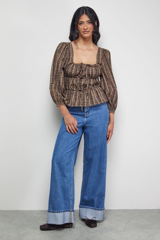 Elegant square neckline with charming tie-front detail
        Voluminous balloon sleeves for a dramatic silhouette
        Fitted smocked bodice creating a flattering shape
        Classic check pattern offering timeless appeal
        Peplum-style hem adding feminine flair to your outfit
    
    This Warehouse blouse combines vintage-inspired charm with contemporary styling. The square neckline frames your dcolletage beautifully, while the tie-front detail adds a touch of playful femininity. The smocked bodice creates definition at the waist, contrasting perfectly with the billowing sleeves for a balanced silhouette. Style with wide-leg jeans and ankle boots for casual weekend brunches, or tuck into a high-waisted midi skirt for family gatherings. For a more polished daytime look, pair with tailored trousers and loafers. The versatile check pattern works brilliantly across seasons - layer under a cardigan when temperatures drop or wear alone for warmer days. This blouse effortlessly bridges the gap between casual comfort and put-together style, making it a wardrobe essential for the confident woman.