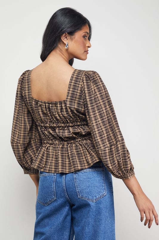 Elegant square neckline with charming tie-front detail
        Voluminous balloon sleeves for a dramatic silhouette
        Fitted smocked bodice creating a flattering shape
        Classic check pattern offering timeless appeal
        Peplum-style hem adding feminine flair to your outfit
    
    This Warehouse blouse combines vintage-inspired charm with contemporary styling. The square neckline frames your dcolletage beautifully, while the tie-front detail adds a touch of playful femininity. The smocked bodice creates definition at the waist, contrasting perfectly with the billowing sleeves for a balanced silhouette. Style with wide-leg jeans and ankle boots for casual weekend brunches, or tuck into a high-waisted midi skirt for family gatherings. For a more polished daytime look, pair with tailored trousers and loafers. The versatile check pattern works brilliantly across seasons - layer under a cardigan when temperatures drop or wear alone for warmer days. This blouse effortlessly bridges the gap between casual comfort and put-together style, making it a wardrobe essential for the confident woman.