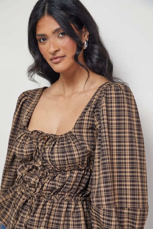Elegant square neckline with charming tie-front detail
        Voluminous balloon sleeves for a dramatic silhouette
        Fitted smocked bodice creating a flattering shape
        Classic check pattern offering timeless appeal
        Peplum-style hem adding feminine flair to your outfit
    
    This Warehouse blouse combines vintage-inspired charm with contemporary styling. The square neckline frames your dcolletage beautifully, while the tie-front detail adds a touch of playful femininity. The smocked bodice creates definition at the waist, contrasting perfectly with the billowing sleeves for a balanced silhouette. Style with wide-leg jeans and ankle boots for casual weekend brunches, or tuck into a high-waisted midi skirt for family gatherings. For a more polished daytime look, pair with tailored trousers and loafers. The versatile check pattern works brilliantly across seasons - layer under a cardigan when temperatures drop or wear alone for warmer days. This blouse effortlessly bridges the gap between casual comfort and put-together style, making it a wardrobe essential for the confident woman.