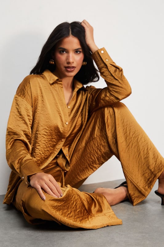 Distinctive hammered satin texture creates a luxe, tactile finish
        Oversized silhouette with dropped shoulders for effortless drape
        Classic collar and button-through front for versatile styling options
        Wide, relaxed sleeves with buttoned cuffs for added comfort
        Generous length perfect for layering or wearing as a standalone piece
    
    This Warehouse hammered satin shirt redefines casual sophistication with its sumptuous texture and relaxed fit. The oversized design creates a contemporary silhouette that's both comfortable and fashion-forward, whilst the lustrous finish adds a touch of understated glamour to everyday ensembles. Style it half-tucked into wide-leg trousers as shown for a coordinated look that transitions seamlessly from day to evening. For casual outings, pair with your favourite denim and trainers, or dress it up with tailored trousers and statement jewellery for dinner dates. The versatile nature of this piece makes it ideal for layering during cooler months or wearing alone when temperatures rise. Machine washable and crafted from cotton, this shirt combines practicality with Warehouse's signature confident, feminine aesthetic.