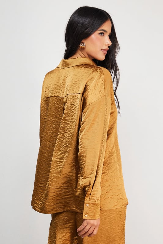 Distinctive hammered satin texture creates a luxe, tactile finish
        Oversized silhouette with dropped shoulders for effortless drape
        Classic collar and button-through front for versatile styling options
        Wide, relaxed sleeves with buttoned cuffs for added comfort
        Generous length perfect for layering or wearing as a standalone piece
    
    This Warehouse hammered satin shirt redefines casual sophistication with its sumptuous texture and relaxed fit. The oversized design creates a contemporary silhouette that's both comfortable and fashion-forward, whilst the lustrous finish adds a touch of understated glamour to everyday ensembles. Style it half-tucked into wide-leg trousers as shown for a coordinated look that transitions seamlessly from day to evening. For casual outings, pair with your favourite denim and trainers, or dress it up with tailored trousers and statement jewellery for dinner dates. The versatile nature of this piece makes it ideal for layering during cooler months or wearing alone when temperatures rise. Machine washable and crafted from cotton, this shirt combines practicality with Warehouse's signature confident, feminine aesthetic.