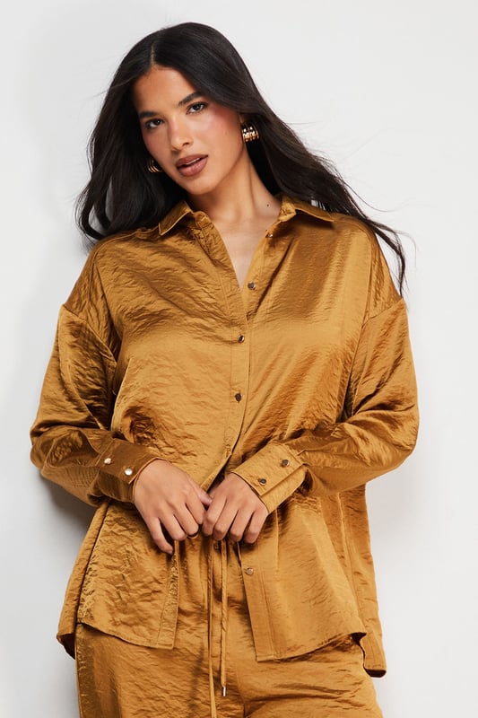 Distinctive hammered satin texture creates a luxe, tactile finish
        Oversized silhouette with dropped shoulders for effortless drape
        Classic collar and button-through front for versatile styling options
        Wide, relaxed sleeves with buttoned cuffs for added comfort
        Generous length perfect for layering or wearing as a standalone piece
    
    This Warehouse hammered satin shirt redefines casual sophistication with its sumptuous texture and relaxed fit. The oversized design creates a contemporary silhouette that's both comfortable and fashion-forward, whilst the lustrous finish adds a touch of understated glamour to everyday ensembles. Style it half-tucked into wide-leg trousers as shown for a coordinated look that transitions seamlessly from day to evening. For casual outings, pair with your favourite denim and trainers, or dress it up with tailored trousers and statement jewellery for dinner dates. The versatile nature of this piece makes it ideal for layering during cooler months or wearing alone when temperatures rise. Machine washable and crafted from cotton, this shirt combines practicality with Warehouse's signature confident, feminine aesthetic.