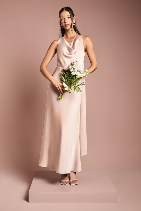 Elegant cowl neckline creates a graceful drape across the dcolletage
        Luxurious satin fabric with a subtle sheen catches the light beautifully
        Flowing chiffon drape detail adds movement and romantic flair
        Sleeveless design offers comfort whilst maintaining a sophisticated silhouette
        Ankle-length cut with a gentle flare creates an effortlessly elegant profile
    
    This stunning Coast bridesmaids dress combines timeless elegance with contemporary design elements. The sumptuous satin fabric creates a sleek silhouette whilst the cowl neckline adds a touch of classic sophistication. The chiffon drape detail flows gracefully from the back, creating movement and dimension as you walk down the aisle. Perfect for your role in the bridal party, this dress can be styled with delicate drop earrings and strappy heeled sandals as shown for a coordinated look that complements the bride without overshadowing her. The clean lines and fluid silhouette ensure comfort throughout the ceremony and reception, allowing you to focus on supporting the bride on her special day. Complete your bridesmaids ensemble with a small posy that echoes the bridal bouquet for a harmonious wedding party aesthetic.