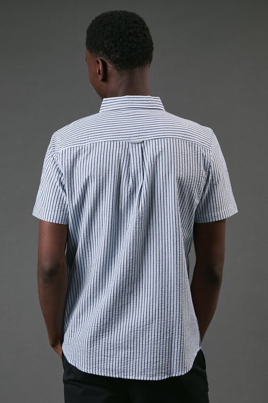 Classic button-down collar for a smart-casual finish
        Distinctive seersucker fabric with textured multi-stripe pattern
        Practical chest pocket with Maine brand detailing
        Short sleeves with neat hems for warm-weather comfort
        Box pleat at back for enhanced movement and fit
    
    This Maine seersucker shirt combines timeless style with practical warm-weather design. The textured multi-stripe pattern creates visual interest while the lightweight woven fabric offers breathability perfect for summer days. Style with dark chinos and white trainers for a relaxed weekend look, as shown, or pair with tailored shorts and loafers for garden parties and casual gatherings. The versatile button-down design transitions effortlessly from daytime outings to evening barbecues. For a layered approach, wear unbuttoned over a plain t-shirt with rolled sleeves. The classic fit provides comfortable movement without sacrificing style, making this shirt an essential addition to your casual wardrobe that will serve you well through numerous summer seasons.