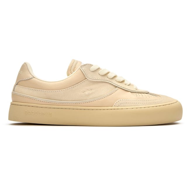 The Good News Lagoon trainers blend retro court styling with eco-conscious craftsmanship. These sand-colored kicks showcase handmade deadstock suede uppers with a distinctive stamped GN motif that adds subtle branding. The chunky organic cotton laces provide a textural contrast against the soft suede, while recycled mesh lining ensures breathable comfort. Perfect for the environmentally mindful gentleman seeking casual footwear with substance, these rubber-soled trainers deliver on both sustainability and laid-back style.