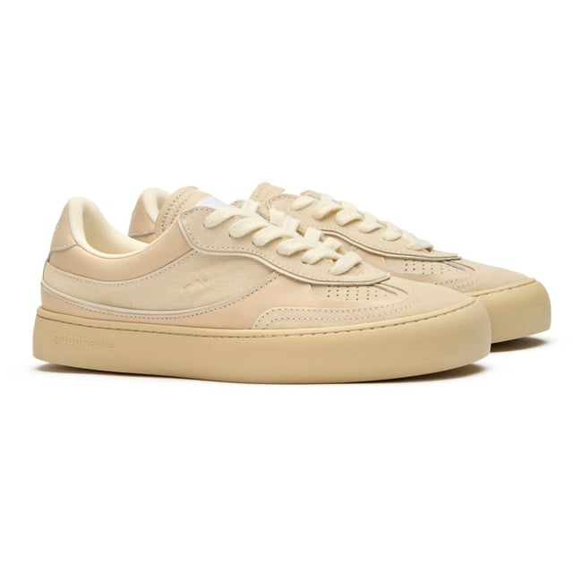 The Good News Lagoon trainers blend retro court styling with eco-conscious craftsmanship. These sand-colored kicks showcase handmade deadstock suede uppers with a distinctive stamped GN motif that adds subtle branding. The chunky organic cotton laces provide a textural contrast against the soft suede, while recycled mesh lining ensures breathable comfort. Perfect for the environmentally mindful gentleman seeking casual footwear with substance, these rubber-soled trainers deliver on both sustainability and laid-back style.