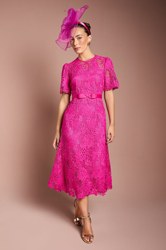 Exquisite lace midi dress with intricate floral pattern
        Elegant bow belt accentuates the waistline
        Flattering round neckline and short sleeves
        Scalloped hem adds a delicate touch
        Midi length perfect for formal occasions
    
    This stunning lace midi dress radiates sophistication and grace, making it an ideal choice for weddings, races, or any formal event where you want to make a lasting impression. The intricate floral lace pattern adorns the entire dress, creating a romantic and feminine silhouette. The bow belt cinches the waist beautifully, enhancing your figure and adding a charming detail. Style this dress with a matching fascinator, as shown, for a coordinated look that's sure to turn heads. Pair with strappy metallic heels and a clutch bag to complete your ensemble. For cooler evenings, drape a lightweight pashmina over your shoulders. This versatile piece can be dressed up or down, making it a valuable addition to your occasion wear wardrobe.