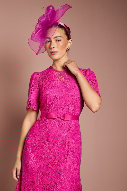 Exquisite lace midi dress with intricate floral pattern
        Elegant bow belt accentuates the waistline
        Flattering round neckline and short sleeves
        Scalloped hem adds a delicate touch
        Midi length perfect for formal occasions
    
    This stunning lace midi dress radiates sophistication and grace, making it an ideal choice for weddings, races, or any formal event where you want to make a lasting impression. The intricate floral lace pattern adorns the entire dress, creating a romantic and feminine silhouette. The bow belt cinches the waist beautifully, enhancing your figure and adding a charming detail. Style this dress with a matching fascinator, as shown, for a coordinated look that's sure to turn heads. Pair with strappy metallic heels and a clutch bag to complete your ensemble. For cooler evenings, drape a lightweight pashmina over your shoulders. This versatile piece can be dressed up or down, making it a valuable addition to your occasion wear wardrobe.