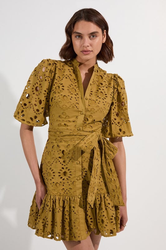 This Karen Millen cotton broderie mini dress combines timeless charm with contemporary styling. The breathable fabric ensures comfort for all-day wear, whilst the intricate eyelet detailing adds texture and visual interest. Style with leather sandals and a woven basket bag for a casual summer look or with espadrille wedges and delicate gold jewellery for elevated occasions. The adjustable tie waist allows for a customised fit, making this piece a flattering addition to your warm-weather wardrobe.  Intricate broderie anglaise pattern Collared neckline with button-down front detail Flutter sleeves Adjustable tie waist Playful ruffle hem detail