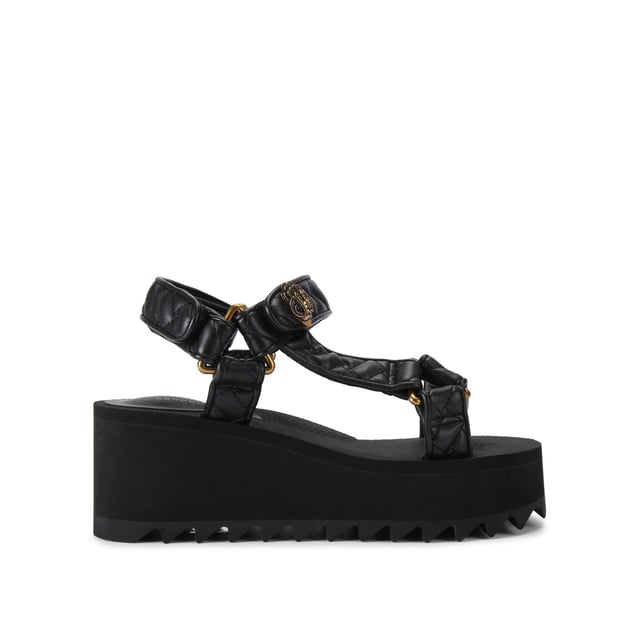 This Kurt Geiger Orion Pump sandal sits on a chunky black sole with exaggerated tread. The upper is in a black overstitch quilted leather alternative. The straps are fastened with velcro topped with an antiqued brass eagle head. Sole height: 7cm.