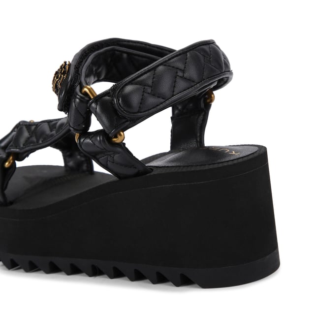 This Kurt Geiger Orion Pump sandal sits on a chunky black sole with exaggerated tread. The upper is in a black overstitch quilted leather alternative. The straps are fastened with velcro topped with an antiqued brass eagle head. Sole height: 7cm.