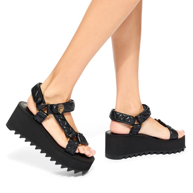 This Kurt Geiger Orion Pump sandal sits on a chunky black sole with exaggerated tread. The upper is in a black overstitch quilted leather alternative. The straps are fastened with velcro topped with an antiqued brass eagle head. Sole height: 7cm.