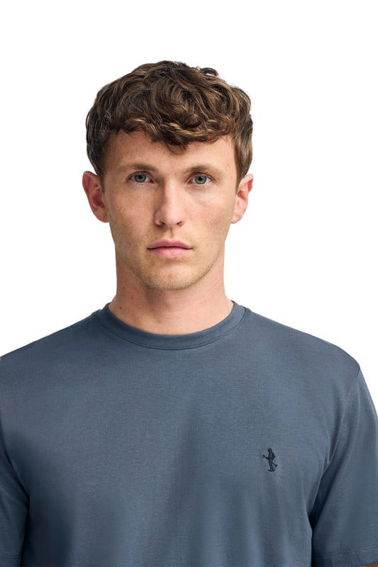Dieses markante T-Shirt mit kurzen Ärmeln definiert das Konzept des Basic neu. Sein Baumwollstoff bietet ein angenehmes und atmungsaktives Tragegefühl, das sich ideal für den Alltag eignet. Die reguläre Passform und der gerippte Rundhalskragen sorgen für einen tadellosen Sitz. Details wie das farblich abgestimmte Nahtband und die exklusive, in dem ikonischen Rigby Go Logo inspirierte Rigby Best Stickerei auf der Brust verleihen ihm einen stilvollen Charakter.
