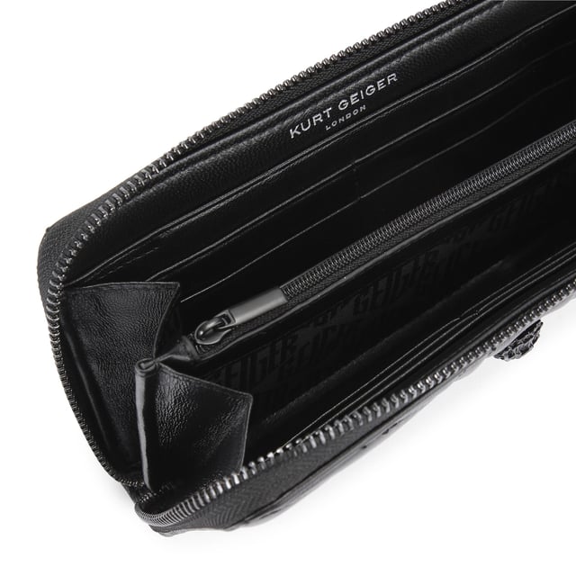 This Kurt Geiger Union Jack Drench Zip Around Purse features a black leather exterior with overstitch quilting creating a Union Jack design. There is a black eagle head with crystals on the front. Dimensions: 10cm (H), 19cm (L), 2cm (D).