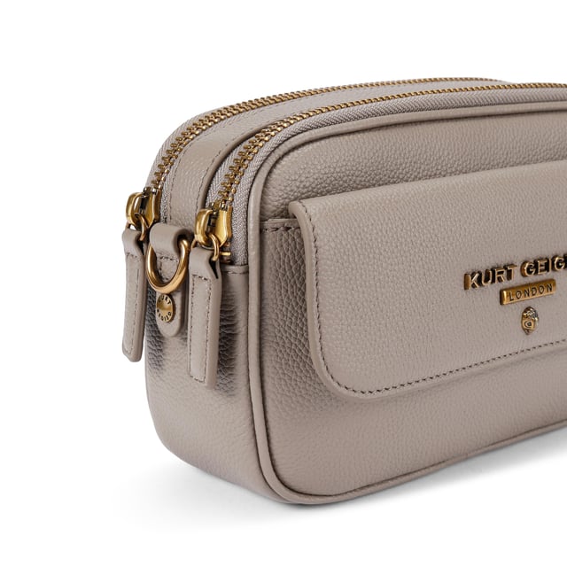 This Kurt Geiger 2Zip Greenwich Cross Body bag is crafted in a taupe grained leather. There is a flat pocket on the back and a magnetic snap closure pocket on the front. There is antiqued brass branding on the front flap. Dimensions: 14cm (H), 23cm (L), 7cm(D). Strap length: 132cm.