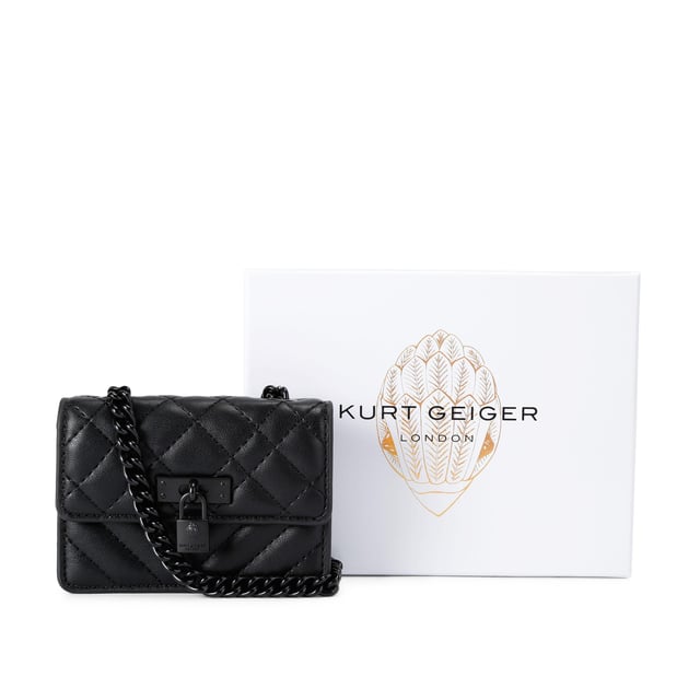 This Kurt Geiger Micro Drench Brixton bag features a black leather alternative exterior with overstitch quilting on the exterior. There is an antiqued brass branded lock on the front flap. Dimensions: 7.5cm (H), 11cm (L), 3cm (D). Strap length: 121cm.