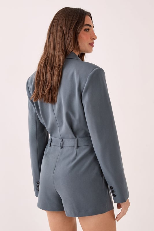 Tailored romper featuring a sophisticated wrap-style front with button detail closure
        Structured blazer-inspired lapel collar adds a smart, professional edge
        Long sleeves with subtle button cuffs for refined detailing
        Defined waistline creates a flattering silhouette
        Fully lined for comfort and smooth wear
    
    Make a statement in this striking tailored romper that seamlessly blends sophistication with contemporary style. The blazer-inspired design with its structured lapels and wrap-front detail creates a polished look that commands attention. Perfect for smart casual events where you want to showcase your fashion-forward sensibilities whilst maintaining an air of refinement. Style with knee-high boots for an evening out, or dress it down with chunky trainers for a modern daytime ensemble. For more formal occasions, pair with strappy heels and statement jewellery to enhance its elegant appeal. The versatile design transitions effortlessly from office to evening drinks, making it an essential addition to your wardrobe. This NastyGal piece offers the perfect balance of comfort and style for the fashion-conscious woman who isn't afraid to stand out.
