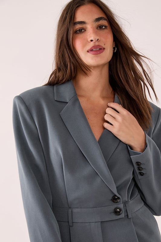 Tailored romper featuring a sophisticated wrap-style front with button detail closure
        Structured blazer-inspired lapel collar adds a smart, professional edge
        Long sleeves with subtle button cuffs for refined detailing
        Defined waistline creates a flattering silhouette
        Fully lined for comfort and smooth wear
    
    Make a statement in this striking tailored romper that seamlessly blends sophistication with contemporary style. The blazer-inspired design with its structured lapels and wrap-front detail creates a polished look that commands attention. Perfect for smart casual events where you want to showcase your fashion-forward sensibilities whilst maintaining an air of refinement. Style with knee-high boots for an evening out, or dress it down with chunky trainers for a modern daytime ensemble. For more formal occasions, pair with strappy heels and statement jewellery to enhance its elegant appeal. The versatile design transitions effortlessly from office to evening drinks, making it an essential addition to your wardrobe. This NastyGal piece offers the perfect balance of comfort and style for the fashion-conscious woman who isn't afraid to stand out.