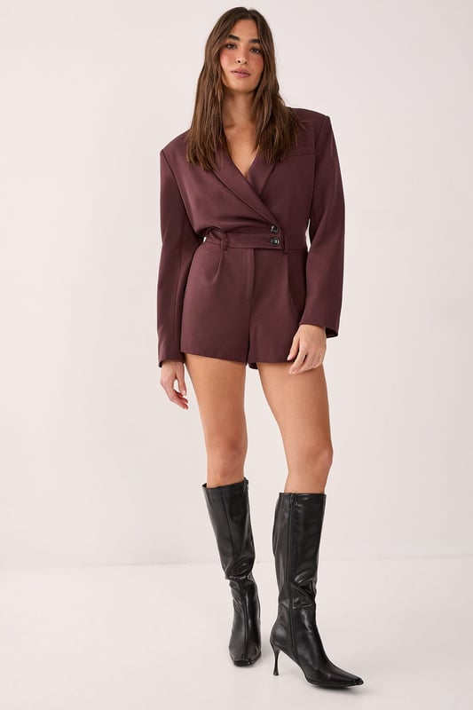 Tailored romper featuring a sophisticated wrap-style front with button detail closure
        Structured blazer-inspired lapel collar adds a smart, professional edge
        Long sleeves with subtle button cuffs for refined detailing
        Defined waistline creates a flattering silhouette
        Fully lined for comfort and smooth wear
    
    Make a statement in this striking tailored romper that seamlessly blends sophistication with contemporary style. The blazer-inspired design with its structured lapels and wrap-front detail creates a polished look that commands attention. Perfect for smart casual events where you want to showcase your fashion-forward sensibilities whilst maintaining an air of refinement. Style with knee-high boots for an evening out, or dress it down with chunky trainers for a modern daytime ensemble. For more formal occasions, pair with strappy heels and statement jewellery to enhance its elegant appeal. The versatile design transitions effortlessly from office to evening drinks, making it an essential addition to your wardrobe. This NastyGal piece offers the perfect balance of comfort and style for the fashion-conscious woman who isn't afraid to stand out.