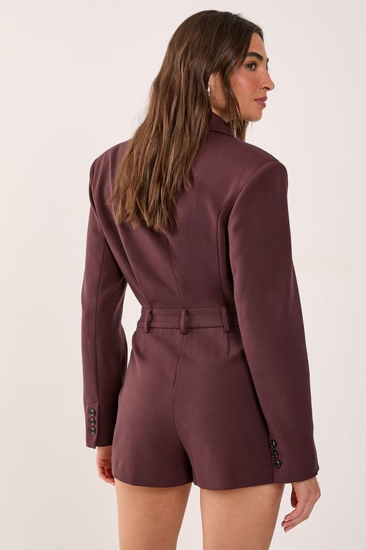 Tailored romper featuring a sophisticated wrap-style front with button detail closure
        Structured blazer-inspired lapel collar adds a smart, professional edge
        Long sleeves with subtle button cuffs for refined detailing
        Defined waistline creates a flattering silhouette
        Fully lined for comfort and smooth wear
    
    Make a statement in this striking tailored romper that seamlessly blends sophistication with contemporary style. The blazer-inspired design with its structured lapels and wrap-front detail creates a polished look that commands attention. Perfect for smart casual events where you want to showcase your fashion-forward sensibilities whilst maintaining an air of refinement. Style with knee-high boots for an evening out, or dress it down with chunky trainers for a modern daytime ensemble. For more formal occasions, pair with strappy heels and statement jewellery to enhance its elegant appeal. The versatile design transitions effortlessly from office to evening drinks, making it an essential addition to your wardrobe. This NastyGal piece offers the perfect balance of comfort and style for the fashion-conscious woman who isn't afraid to stand out.