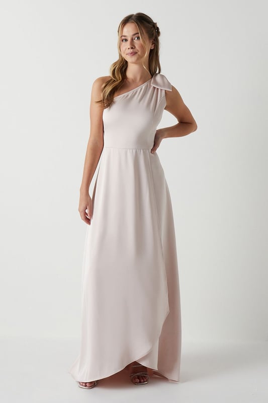 Elegant one shoulder design with a sophisticated bow detail
        Flowing satin fabric that drapes beautifully for a graceful silhouette
        Flattering fitted bodice transitioning into a floor-length skirt
        Subtle wrap-effect hemline creating movement and dimension
        Designed specifically for bridesmaids to complement the bridal party
    
    This enchanting Coast bridesmaids dress combines timeless elegance with contemporary design. The one shoulder neckline with its delicate bow detail creates a refined asymmetric look that photographs beautifully from every angle. The fitted bodice gently hugs your figure before flowing into a graceful floor-length skirt with a subtle wrap effect that adds movement as you walk down the aisle. Perfect for the bridal party, this dress can be styled with delicate jewellery and an elegant updo to mirror the model's sophisticated half-up hairstyle. Complete your bridesmaids look with strappy heels and a small clutch that coordinates with the wedding colour scheme. The satin fabric catches the light beautifully, ensuring you'll shine in your supporting role on the special day whilst maintaining the perfect balance of sophistication and grace.