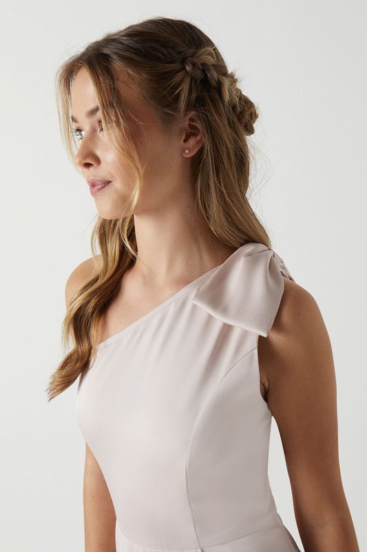 Elegant one shoulder design with a sophisticated bow detail
        Flowing satin fabric that drapes beautifully for a graceful silhouette
        Flattering fitted bodice transitioning into a floor-length skirt
        Subtle wrap-effect hemline creating movement and dimension
        Designed specifically for bridesmaids to complement the bridal party
    
    This enchanting Coast bridesmaids dress combines timeless elegance with contemporary design. The one shoulder neckline with its delicate bow detail creates a refined asymmetric look that photographs beautifully from every angle. The fitted bodice gently hugs your figure before flowing into a graceful floor-length skirt with a subtle wrap effect that adds movement as you walk down the aisle. Perfect for the bridal party, this dress can be styled with delicate jewellery and an elegant updo to mirror the model's sophisticated half-up hairstyle. Complete your bridesmaids look with strappy heels and a small clutch that coordinates with the wedding colour scheme. The satin fabric catches the light beautifully, ensuring you'll shine in your supporting role on the special day whilst maintaining the perfect balance of sophistication and grace.