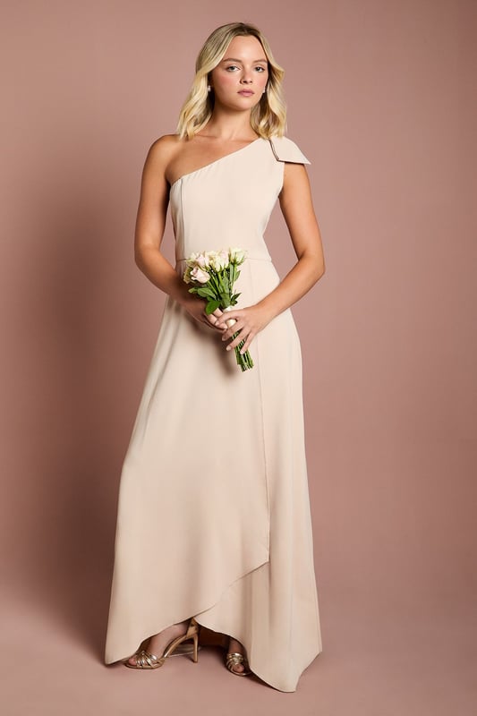 Elegant one shoulder design with a sophisticated bow detail
        Flowing satin fabric that drapes beautifully for a graceful silhouette
        Flattering fitted bodice transitioning into a floor-length skirt
        Subtle wrap-effect hemline creating movement and dimension
        Designed specifically for bridesmaids to complement the bridal party
    
    This enchanting Coast bridesmaids dress combines timeless elegance with contemporary design. The one shoulder neckline with its delicate bow detail creates a refined asymmetric look that photographs beautifully from every angle. The fitted bodice gently hugs your figure before flowing into a graceful floor-length skirt with a subtle wrap effect that adds movement as you walk down the aisle. Perfect for the bridal party, this dress can be styled with delicate jewellery and an elegant updo to mirror the model's sophisticated half-up hairstyle. Complete your bridesmaids look with strappy heels and a small clutch that coordinates with the wedding colour scheme. The satin fabric catches the light beautifully, ensuring you'll shine in your supporting role on the special day whilst maintaining the perfect balance of sophistication and grace.
