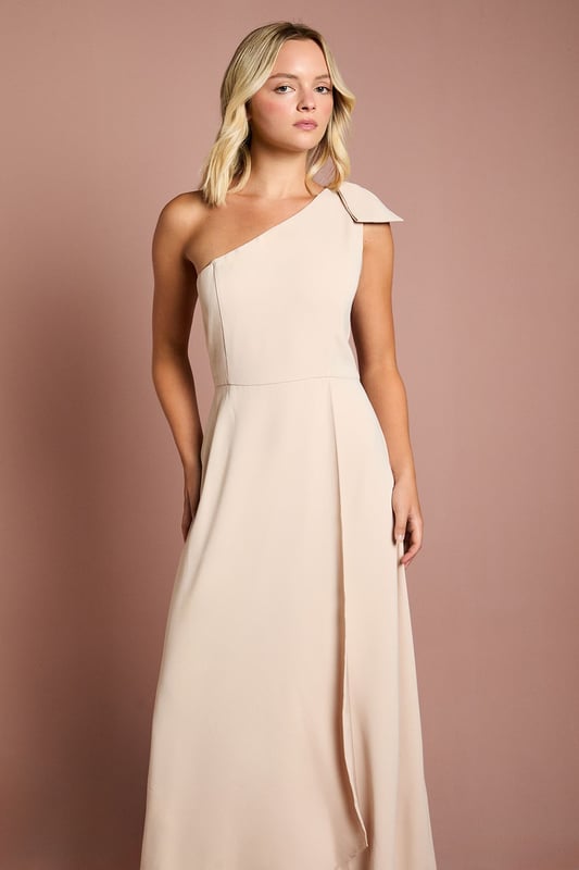 Elegant one shoulder design with a sophisticated bow detail
        Flowing satin fabric that drapes beautifully for a graceful silhouette
        Flattering fitted bodice transitioning into a floor-length skirt
        Subtle wrap-effect hemline creating movement and dimension
        Designed specifically for bridesmaids to complement the bridal party
    
    This enchanting Coast bridesmaids dress combines timeless elegance with contemporary design. The one shoulder neckline with its delicate bow detail creates a refined asymmetric look that photographs beautifully from every angle. The fitted bodice gently hugs your figure before flowing into a graceful floor-length skirt with a subtle wrap effect that adds movement as you walk down the aisle. Perfect for the bridal party, this dress can be styled with delicate jewellery and an elegant updo to mirror the model's sophisticated half-up hairstyle. Complete your bridesmaids look with strappy heels and a small clutch that coordinates with the wedding colour scheme. The satin fabric catches the light beautifully, ensuring you'll shine in your supporting role on the special day whilst maintaining the perfect balance of sophistication and grace.