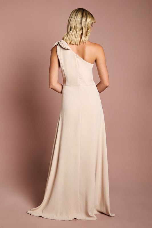 Elegant one shoulder design with a sophisticated bow detail
        Flowing satin fabric that drapes beautifully for a graceful silhouette
        Flattering fitted bodice transitioning into a floor-length skirt
        Subtle wrap-effect hemline creating movement and dimension
        Designed specifically for bridesmaids to complement the bridal party
    
    This enchanting Coast bridesmaids dress combines timeless elegance with contemporary design. The one shoulder neckline with its delicate bow detail creates a refined asymmetric look that photographs beautifully from every angle. The fitted bodice gently hugs your figure before flowing into a graceful floor-length skirt with a subtle wrap effect that adds movement as you walk down the aisle. Perfect for the bridal party, this dress can be styled with delicate jewellery and an elegant updo to mirror the model's sophisticated half-up hairstyle. Complete your bridesmaids look with strappy heels and a small clutch that coordinates with the wedding colour scheme. The satin fabric catches the light beautifully, ensuring you'll shine in your supporting role on the special day whilst maintaining the perfect balance of sophistication and grace.