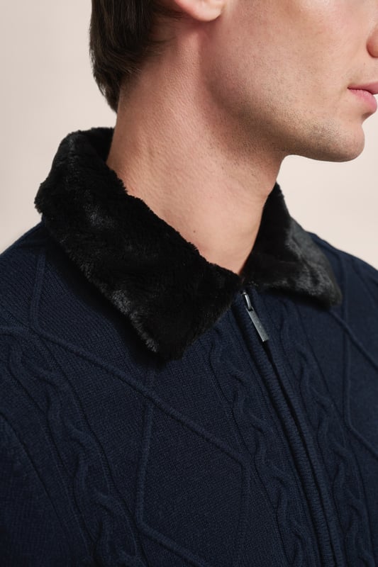 Setze ein modisches Statement mit der bugatti Strickjacke - perfekt für kühle Tage. Diese Jacke aus einem warmen Woll-Mix zeichnet sich durch ihren stilvollen unechten Fellkragen und das attraktive Zopf- und Rautenmuster auf der Vorderseite aus. Ausgestattet mit einem praktischen Reißverschluss und einem komfortablen Umlegekragen, bietet sie eine bequeme Regular-Fit-Passform. Die Rippenbündchen sorgen für einen perfekten Sitz.