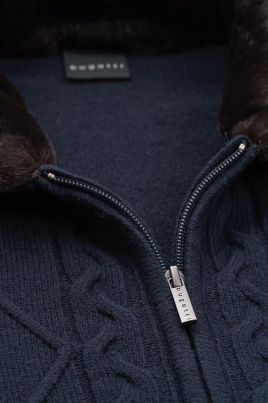 Setze ein modisches Statement mit der bugatti Strickjacke - perfekt für kühle Tage. Diese Jacke aus einem warmen Woll-Mix zeichnet sich durch ihren stilvollen unechten Fellkragen und das attraktive Zopf- und Rautenmuster auf der Vorderseite aus. Ausgestattet mit einem praktischen Reißverschluss und einem komfortablen Umlegekragen, bietet sie eine bequeme Regular-Fit-Passform. Die Rippenbündchen sorgen für einen perfekten Sitz.