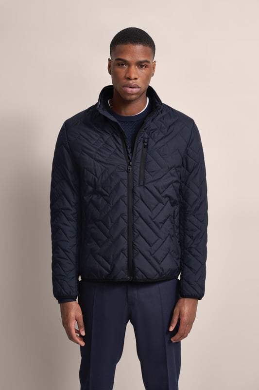 Ervaar het comfort en de stijl van de bugatti blouson in een moderne gewatteerde look. Deze lichtgewicht nylon blouson is ideaal voor op reis en biedt optimaal comfort en warmte met zijn opstaande kraag, gebreide manchetten aan de mouwen en romp en gevoerde voorkant - zonder gebruik van echt dons. Er is ook een praktische zak met rits op de borst!
