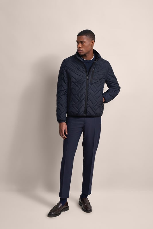 Ervaar het comfort en de stijl van de bugatti blouson in een moderne gewatteerde look. Deze lichtgewicht nylon blouson is ideaal voor op reis en biedt optimaal comfort en warmte met zijn opstaande kraag, gebreide manchetten aan de mouwen en romp en gevoerde voorkant - zonder gebruik van echt dons. Er is ook een praktische zak met rits op de borst!