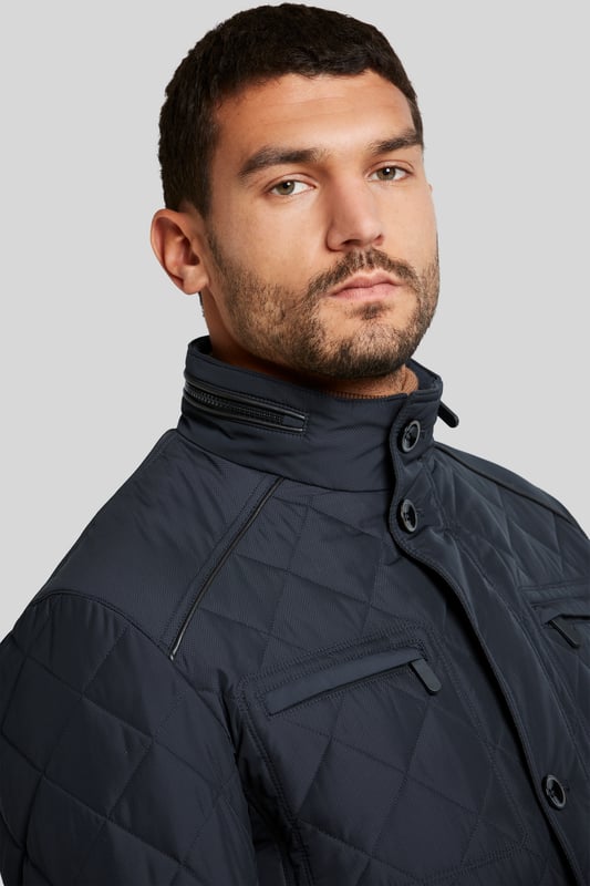 Die moderne Männerjacke im Rautenstepp und mit modernem Stehkragen überzeugt mit aufgesetzten Pattentasche und zwei Brusttaschen. Kunstlederkontraste am Kragen setzen Akzente. Die Jacke besitzt zudem eine funktionale wasserabweisende Funktion.