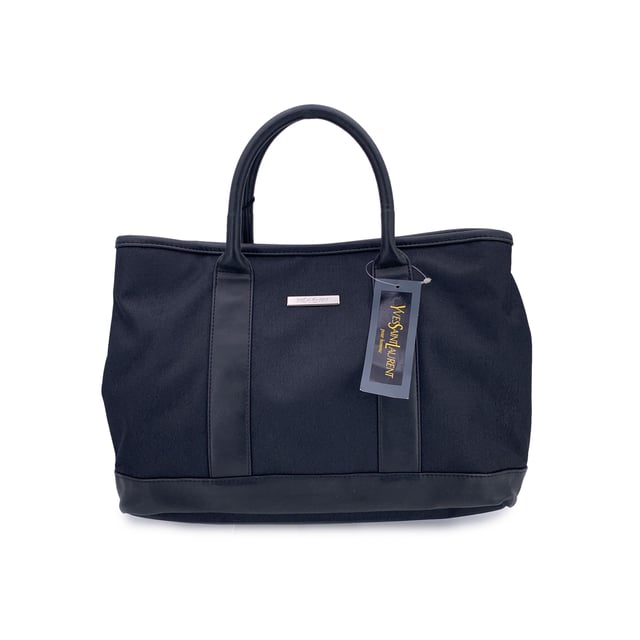 VINTAGE, RRP AS NEW
Understated, refined, and undeniably rare, this Vintage Yves Saint Laurent Pour Homme tote captures the quiet confidence of YSL's menswear line in a form that still feels effortlessly modern. Crafted from durable black nylon canvas and accented with sleek black leather trim, this tote is a functional piece with subtle designer distinction.  At the front, a silver metal Yves Saint Laurent tab adds a discreet touch of luxury, while the magnetic button closure opens to reveal a black nylon canvas lining-clean, simple, and timeless. Inside, a zip pocket offers secure storage, and the original 'Yves Saint Laurent' tag affirms the bag's ity. A true collector's bonus: the 'Yves Saint Laurent Pour Homme' shop hang tag remains thoughtfully attached, hinting at the bag's pristine and possibly unused Condition Rating: A - EXCELLENTCondition Details: Gently used. Yves Saint Laurent hang tag still attached. Please check the photos carefully and ask if you need to know more details or if you have any doubts.Measurements (cm):Depth: 15.2Height: 24.1Length: 35.6Other Details: Dustbag? NoKeys? NoBox? No Measurments:  width: 152 mm length: 356 mm height: 241 mm strap length: 0 mm handle drop: 0 mm