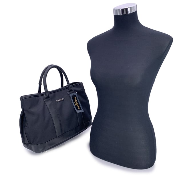 VINTAGE, RRP AS NEW
Understated, refined, and undeniably rare, this Vintage Yves Saint Laurent Pour Homme tote captures the quiet confidence of YSL's menswear line in a form that still feels effortlessly modern. Crafted from durable black nylon canvas and accented with sleek black leather trim, this tote is a functional piece with subtle designer distinction.  At the front, a silver metal Yves Saint Laurent tab adds a discreet touch of luxury, while the magnetic button closure opens to reveal a black nylon canvas lining-clean, simple, and timeless. Inside, a zip pocket offers secure storage, and the original 'Yves Saint Laurent' tag affirms the bag's ity. A true collector's bonus: the 'Yves Saint Laurent Pour Homme' shop hang tag remains thoughtfully attached, hinting at the bag's pristine and possibly unused Condition Rating: A - EXCELLENTCondition Details: Gently used. Yves Saint Laurent hang tag still attached. Please check the photos carefully and ask if you need to know more details or if you have any doubts.Measurements (cm):Depth: 15.2Height: 24.1Length: 35.6Other Details: Dustbag? NoKeys? NoBox? No Measurments:  width: 152 mm length: 356 mm height: 241 mm strap length: 0 mm handle drop: 0 mm