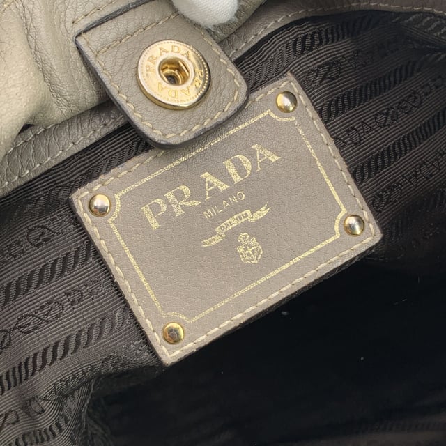 VINTAGE, RRP AS NEW
This beautiful item will come with a Certificate of ity provided by Entrupy. The certificate will be provided at no further cost  Elevate your everyday with this beautiful PRADA tote bag, crafted in luxurious grey taupe textured leather-a timeless neutral that pairs effortlessly with any look. Showcasing PRADA's signature blend of elegance and functionality, this tote features structured double top handles and refined silver-tone Prada lettering on the front, adding a touch of quiet sophistication.  The top opens with a button closure to reveal a spacious main compartment, fully lined in PRADA's iconic jacquard fabric. Inside, you'll find one zip pocket and one open pocket to keep your essentials neatly organized. A 'PRADA Milano' tag and a discreet numbered label tucked inside the interior pocket ensure ity.  Finished with four metal bottom feet for added protection and polish, this tote is as practical as it is chic-perfect for the modern woman who values understated luxury. Condition Rating: B - VERY GOOD CONDITIONCondition Details: Some wear of use on the upper border (please see photos). Some wear of use on the hardware. Please check the photos carefully and ask if you need to know more details or if you have any doubts.Measurements (cm):Depth: 15.2Height: 34.3Length: 36.8Other Details: Dustbag? NoKeys? NoBox? No Measurments:  width: 152 mm length: 368 mm height: 343 mm strap length: 0 mm handle drop: 0 mm