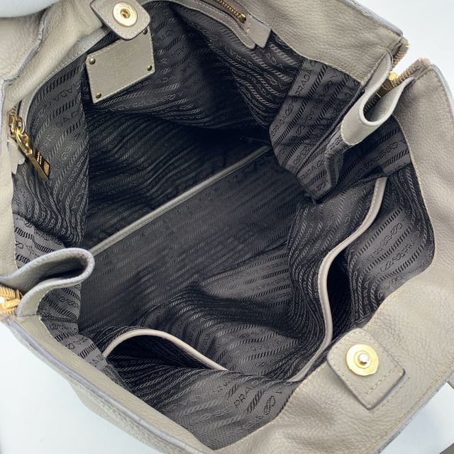 VINTAGE, RRP AS NEW
This beautiful item will come with a Certificate of ity provided by Entrupy. The certificate will be provided at no further cost  Elevate your everyday with this beautiful PRADA tote bag, crafted in luxurious grey taupe textured leather-a timeless neutral that pairs effortlessly with any look. Showcasing PRADA's signature blend of elegance and functionality, this tote features structured double top handles and refined silver-tone Prada lettering on the front, adding a touch of quiet sophistication.  The top opens with a button closure to reveal a spacious main compartment, fully lined in PRADA's iconic jacquard fabric. Inside, you'll find one zip pocket and one open pocket to keep your essentials neatly organized. A 'PRADA Milano' tag and a discreet numbered label tucked inside the interior pocket ensure ity.  Finished with four metal bottom feet for added protection and polish, this tote is as practical as it is chic-perfect for the modern woman who values understated luxury. Condition Rating: B - VERY GOOD CONDITIONCondition Details: Some wear of use on the upper border (please see photos). Some wear of use on the hardware. Please check the photos carefully and ask if you need to know more details or if you have any doubts.Measurements (cm):Depth: 15.2Height: 34.3Length: 36.8Other Details: Dustbag? NoKeys? NoBox? No Measurments:  width: 152 mm length: 368 mm height: 343 mm strap length: 0 mm handle drop: 0 mm