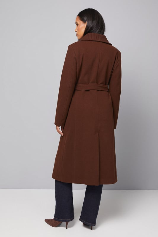 Elegant knitted collar for added sophistication
        Wrap design with button-through closure for versatile styling
        Long length offers maximum coverage and warmth
        Belted waist creates a flattering silhouette
        Functional side pockets for practicality
    
    This Wallis Knitted Collar Button Through Wrap Coat is the epitome of refined elegance. Perfect for the woman who appreciates sophistication without compromising on comfort, this coat is a versatile addition to any wardrobe. The wrap design allows for customisable fit, while the button-through closure adds a touch of classic charm. Style it over a sleek midi dress and pair with heeled boots for a polished look at formal events. For smart casual occasions, layer it over tailored trousers and a fine knit jumper, completing the ensemble with leather ankle boots. The long length and belted waist not only provide warmth but also create a striking silhouette that's sure to turn heads. Whether you're attending a business meeting or heading to a sophisticated dinner, this coat will ensure you look impeccably put-together while feeling effortlessly comfortable.